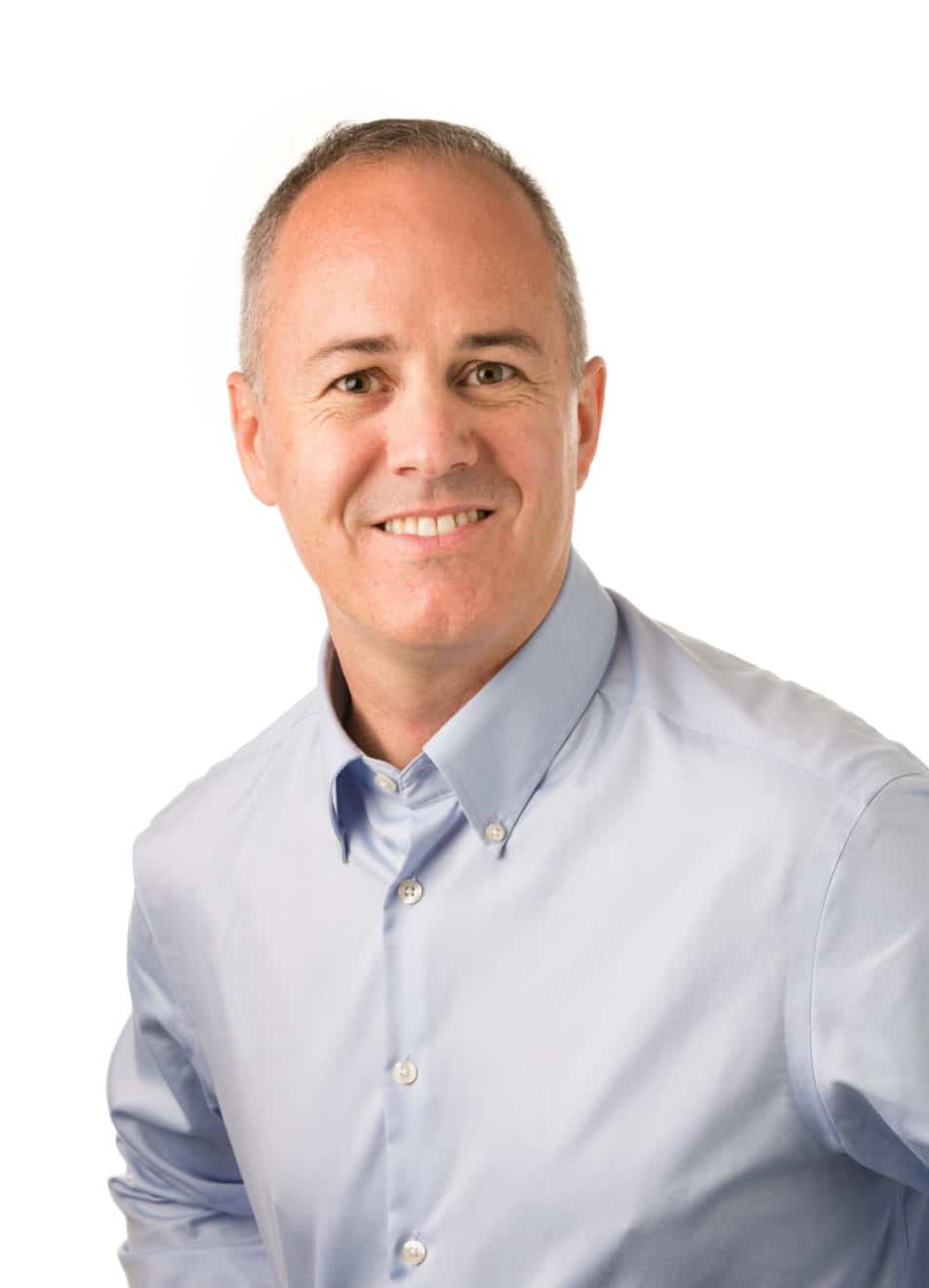 A smiling man with short gray hair, wearing a light blue button-up shirt, poses against a plain white background.
