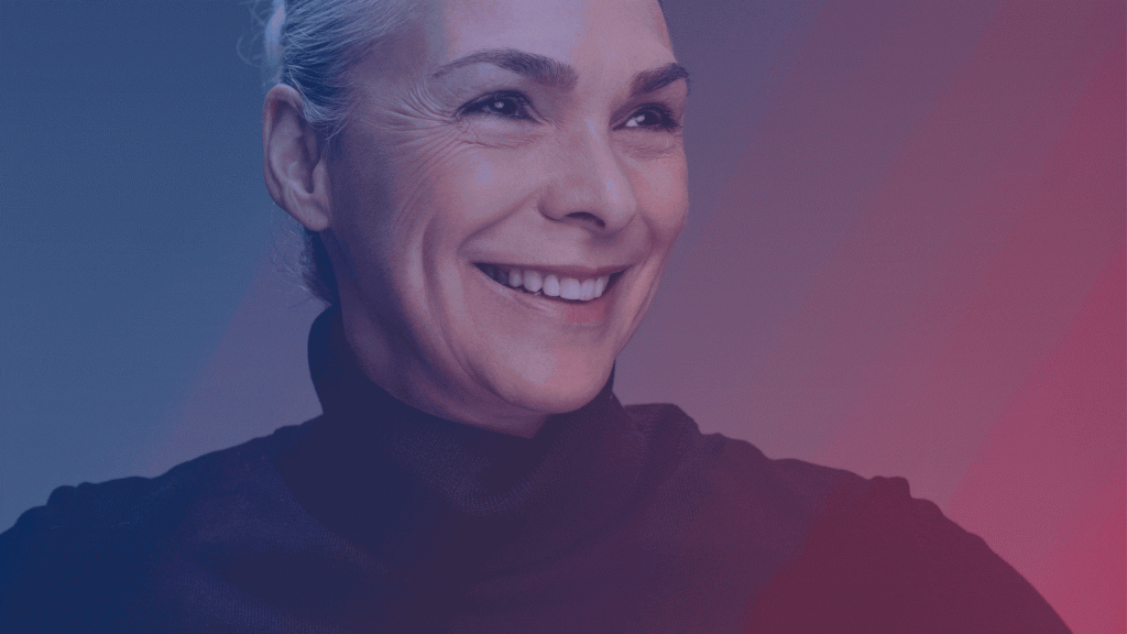 Smiling older woman with light hair pulled back, wearing a dark turtleneck sweater, looking slightly to the side. A blue and pink gradient overlay adds a celebratory touch, perfect for honoring Women's Day.
